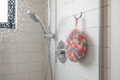 Éponge ronde multicolore au crochet accrochée dans une cabine de douche – accessoire de bain écologique fait main